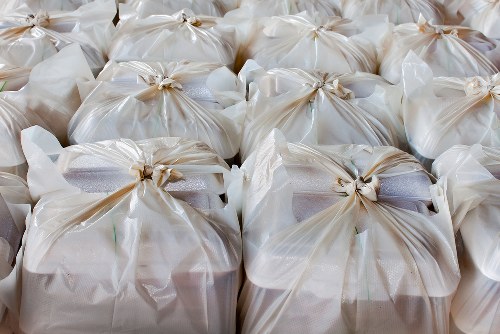 A close-up view of multiple white plastic rubbish bags tightly knotted at the top, filled with waste material, and arranged in neat overlapping rows. The bags are situated on a flat surface, possibly an outdoor pavement or driveway near a commercial or residential property. The surface beneath the bags is not fully visible but appears to be concrete or asphalt. The plastic material of the bags has a glossy finish, reflecting light, and their slightly crinkled texture indicates they are filled with soft or loose rubbish. The background shows more bags extending into the distance, indicating a collection of waste ready for collection or disposal. This scene suggests a professional rubbish collection or waste clearance operation, potentially carried out by services like Commercial Waste Kings Cross, serving the local area in London postcodes associated with Kings Cross.